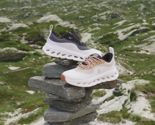 Dva modela superg LOEWE x On Cloudtilt 2.0 postavljena na kamniti sklad v alpski pokrajini – minimalistična silhueta z napredno tehnologijo CloudTec® Phase za blaženje. / Two pairs of LOEWE x On Cloudtilt 2.0 sneakers placed on a stone stack in an alpine landscape – minimalist silhouette with advanced CloudTec® Phase cushioning technology.