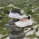 Dva modela superg LOEWE x On Cloudtilt 2.0 postavljena na kamniti sklad v alpski pokrajini – minimalistična silhueta z napredno tehnologijo CloudTec® Phase za blaženje. / Two pairs of LOEWE x On Cloudtilt 2.0 sneakers placed on a stone stack in an alpine landscape – minimalist silhouette with advanced CloudTec® Phase cushioning technology.
