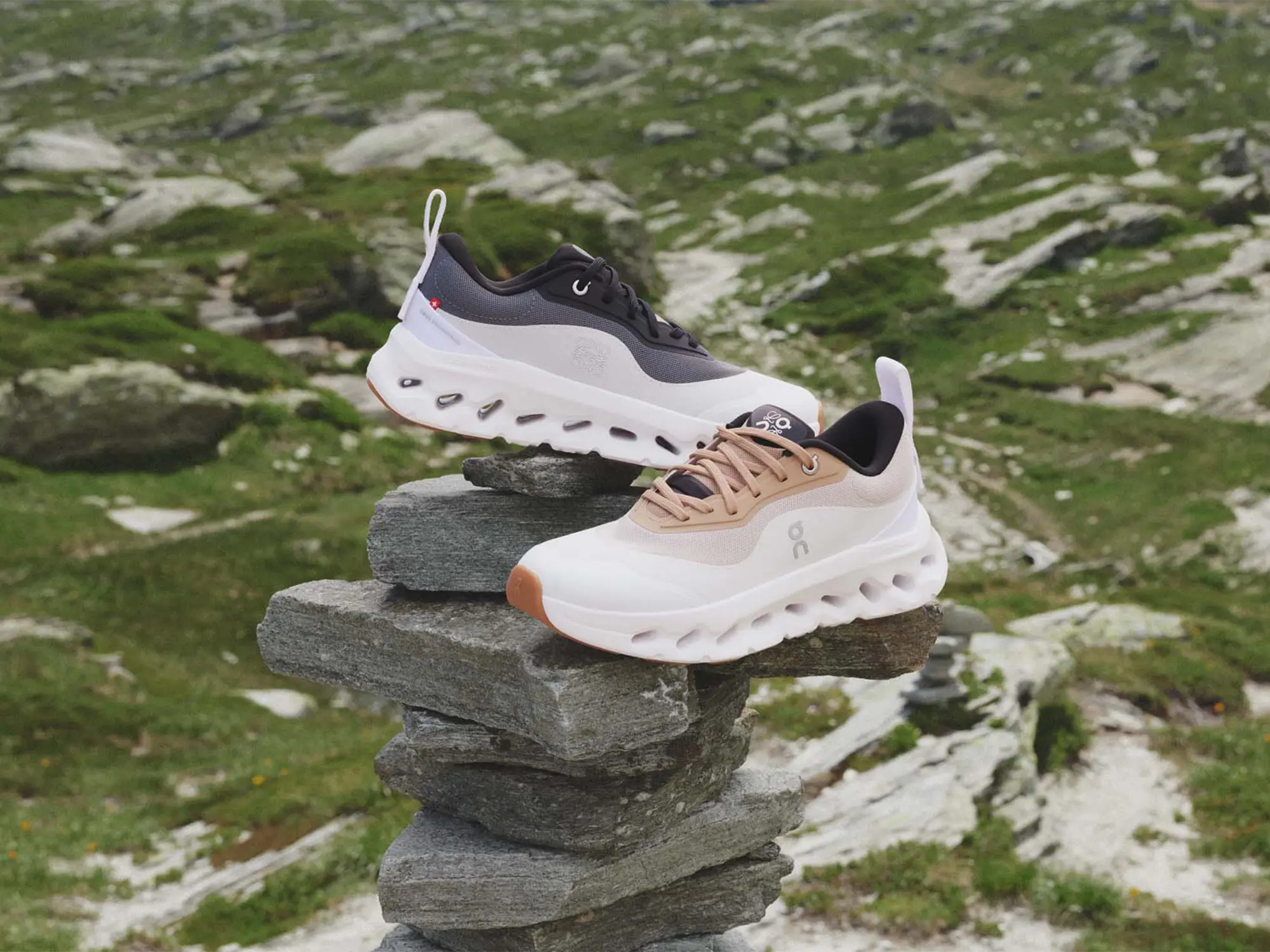 Dva modela superg LOEWE x On Cloudtilt 2.0 postavljena na kamniti sklad v alpski pokrajini – minimalistična silhueta z napredno tehnologijo CloudTec® Phase za blaženje. / Two pairs of LOEWE x On Cloudtilt 2.0 sneakers placed on a stone stack in an alpine landscape – minimalist silhouette with advanced CloudTec® Phase cushioning technology.