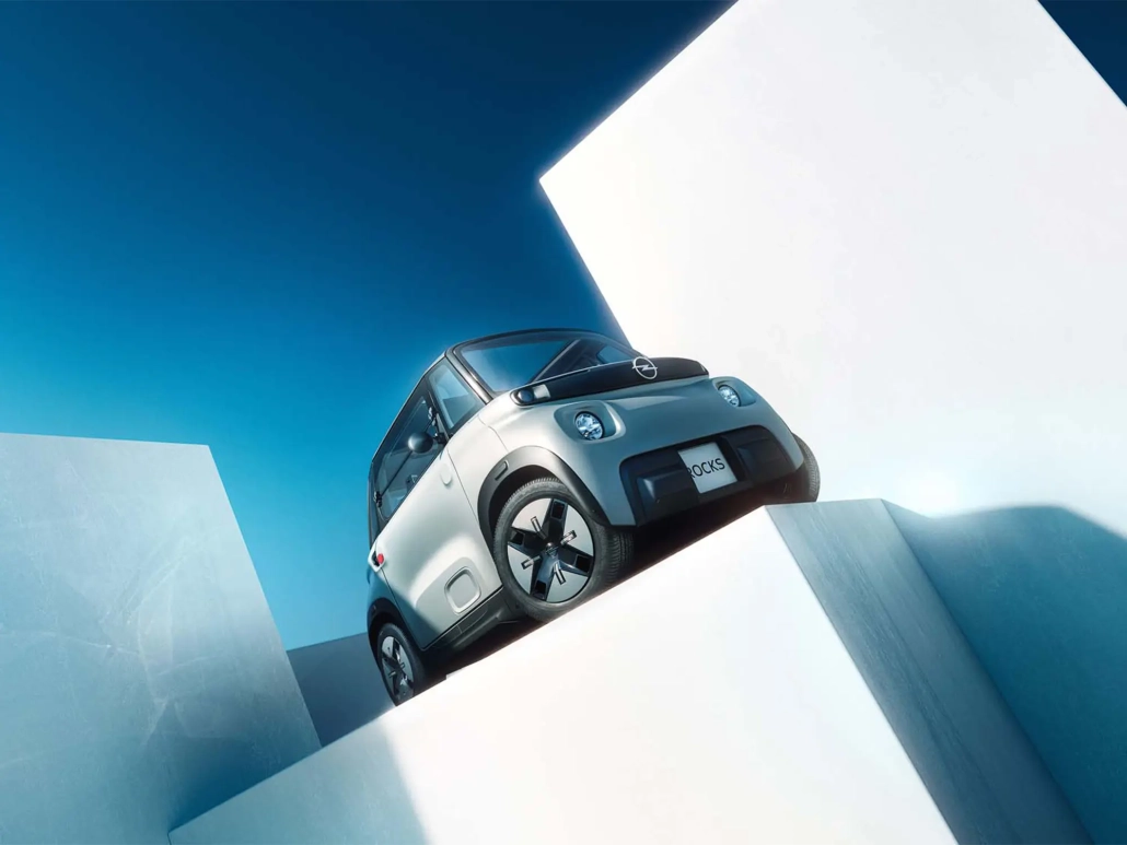 Električni štirikolesnik Opel Rocks v svetlo sivi barvi z novo črno masko Vizor in belim logotipom Blitz, predstavljen kot sodobno urbano vozilo za mlade. (David Magazine for Men with Style) / Opel Rocks electric quadricycle in light grey with new black Vizor grille and white Blitz logo, introduced as a modern urban mobility solution for youth. (David Magazine for Men with Style)