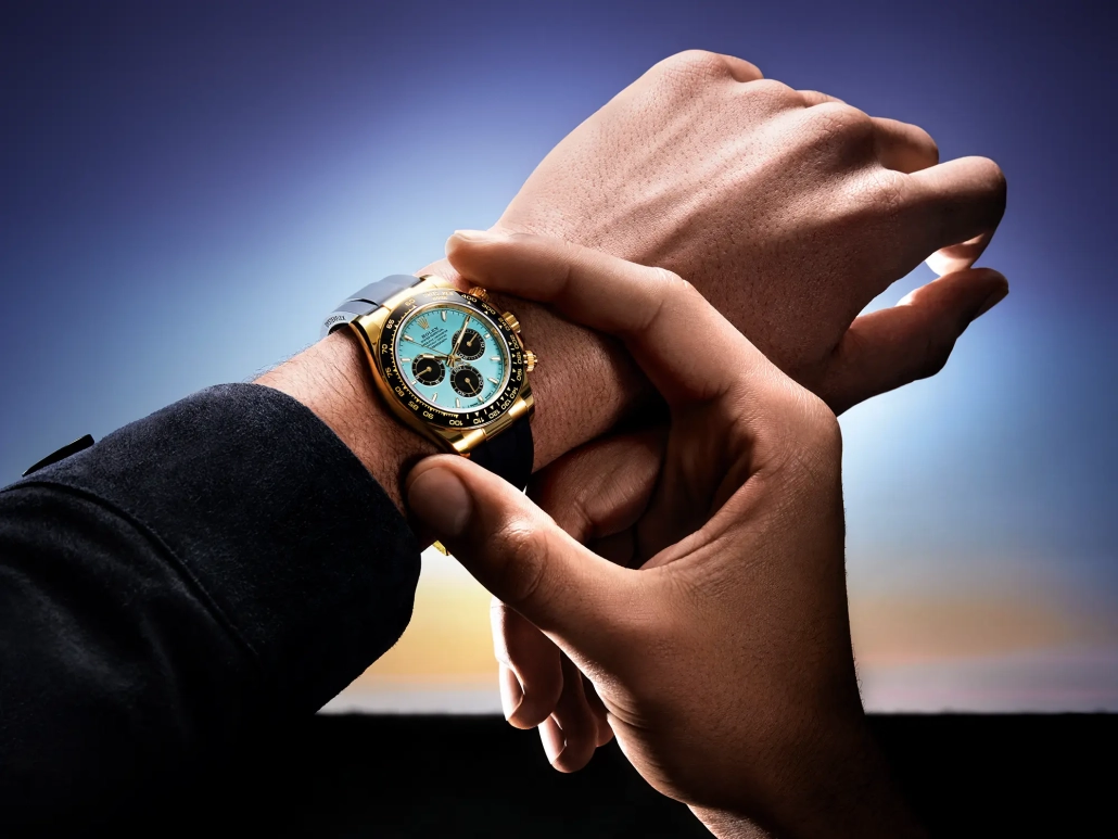 Ura Rolex Oyster Perpetual Cosmograph Daytona z ledeno modro številčnico, kronografskimi števci in 18-karatnim zlatim ohišjem, na črnem Oysterflex paščku – fotografirano v zlati svetlobi sončnega zahoda. (David Magazine for Men with Style) / Rolex Oyster Perpetual Cosmograph Daytona with an ice blue dial, chronograph counters, and 18k gold case on a black Oysterflex strap – photographed in golden sunset light. (David Magazine for Men with Style)
