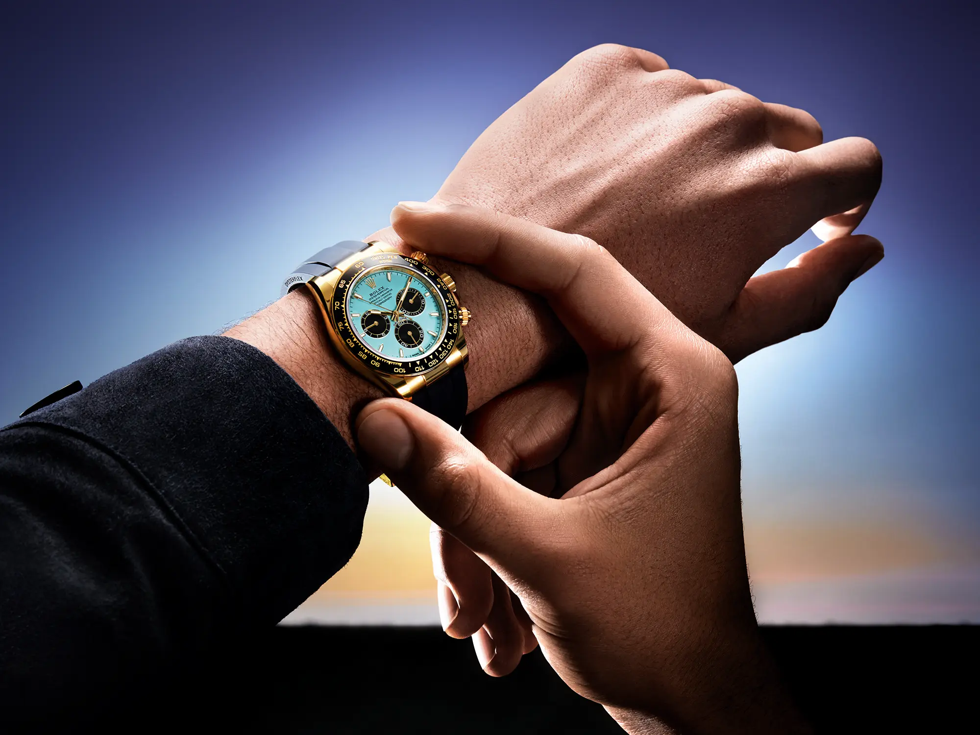 Ura Rolex Oyster Perpetual Cosmograph Daytona z ledeno modro številčnico, kronografskimi števci in 18-karatnim zlatim ohišjem, na črnem Oysterflex paščku – fotografirano v zlati svetlobi sončnega zahoda. (David Magazine for Men with Style) / Rolex Oyster Perpetual Cosmograph Daytona with an ice blue dial, chronograph counters, and 18k gold case on a black Oysterflex strap – photographed in golden sunset light. (David Magazine for Men with Style)