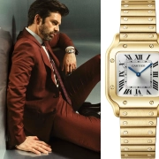 Moški v bordo obleki s prestižno ročno uro Cartier Santos iz rumenega zlata na zapestju, upodobljen v elegantnem ambientu. (David Magazine for Men with Style) / Man in a burgundy suit wearing a prestigious yellow gold Cartier Santos wristwatch, captured in an elegant setting. (David Magazine for Men with Style)