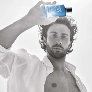Aaron Taylor-Johnson drži stekleničko parfuma Giorgio Armani Acqua Di Giò Profondo Eau de Toilette v svetli, poletni atmosferi – simbol svežine, moškosti in povezave z naravo. / Aaron Taylor-Johnson holding a bottle of Giorgio Armani Acqua Di Giò Profondo Eau de Toilette in a bright summer setting – a symbol of freshness, masculinity, and connection with nature.