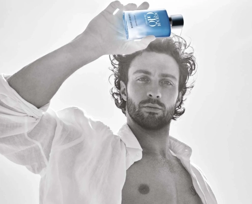 Aaron Taylor-Johnson drži stekleničko parfuma Giorgio Armani Acqua Di Giò Profondo Eau de Toilette v svetli, poletni atmosferi – simbol svežine, moškosti in povezave z naravo. / Aaron Taylor-Johnson holding a bottle of Giorgio Armani Acqua Di Giò Profondo Eau de Toilette in a bright summer setting – a symbol of freshness, masculinity, and connection with nature.
