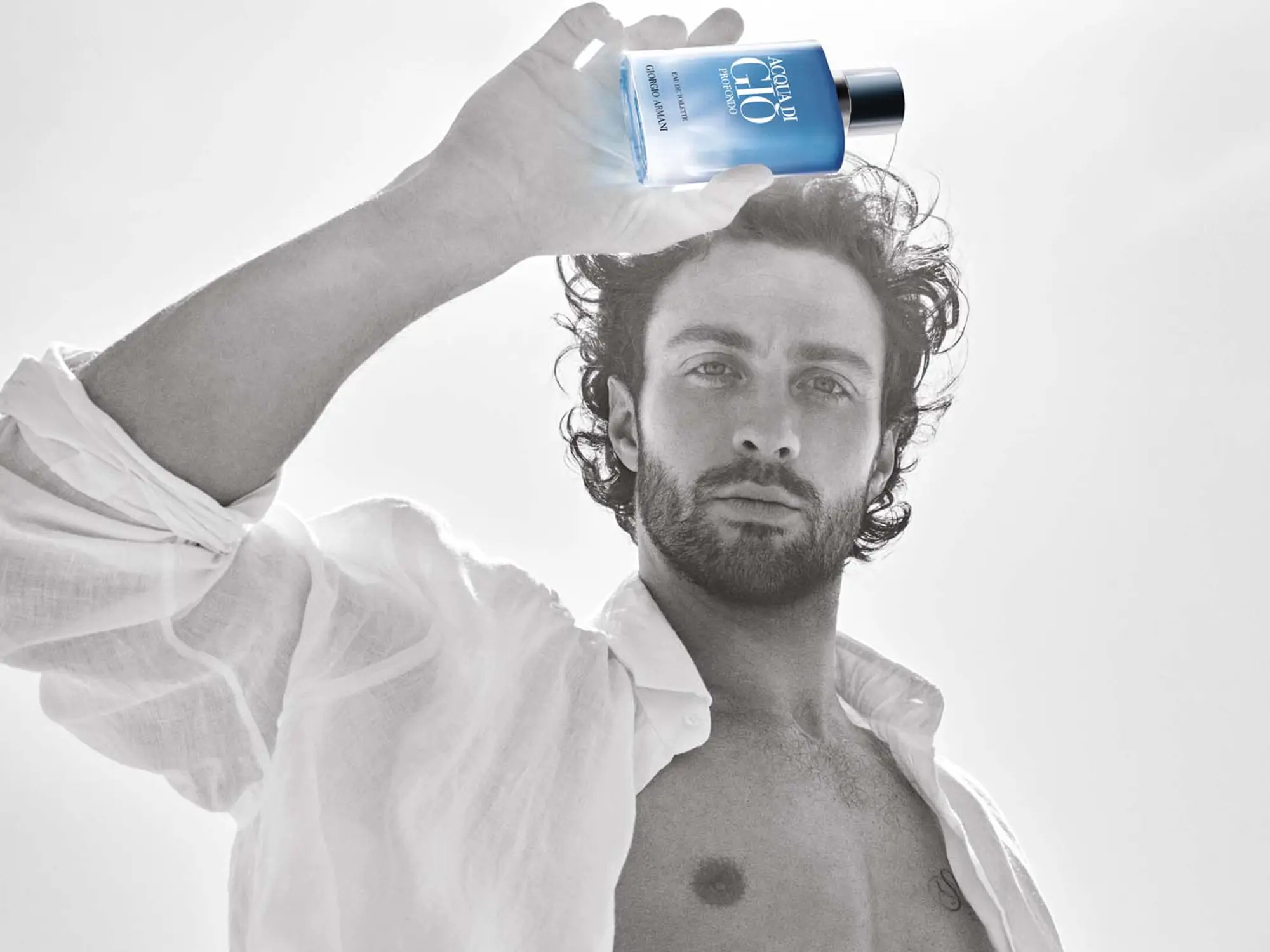 Aaron Taylor-Johnson drži stekleničko parfuma Giorgio Armani Acqua Di Giò Profondo Eau de Toilette v svetli, poletni atmosferi – simbol svežine, moškosti in povezave z naravo. / Aaron Taylor-Johnson holding a bottle of Giorgio Armani Acqua Di Giò Profondo Eau de Toilette in a bright summer setting – a symbol of freshness, masculinity, and connection with nature.