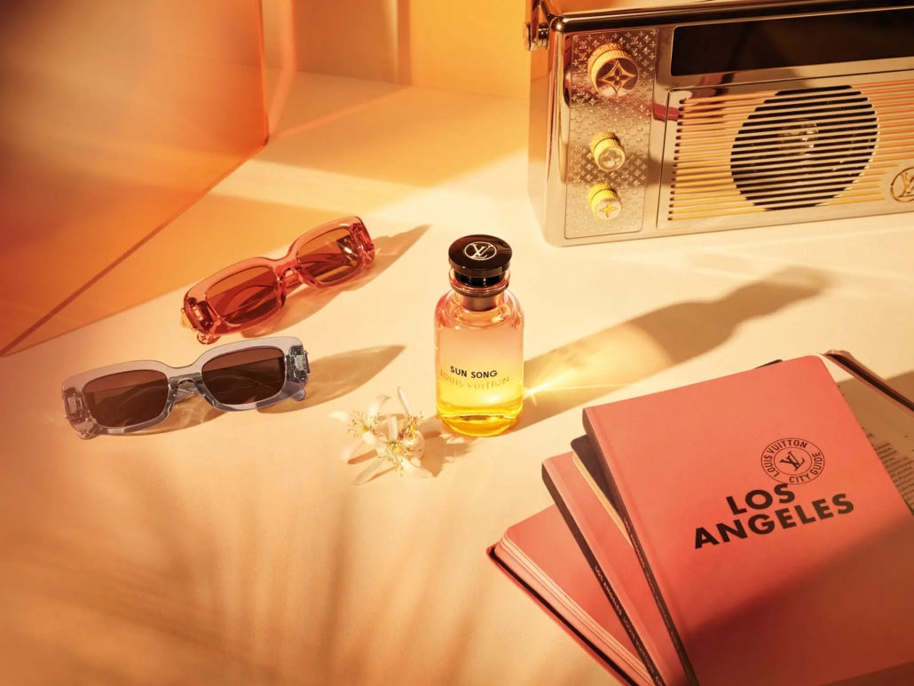 Parfumska voda Louis Vuitton Sun Song s sončno rumeno stekleničko, sončnimi očali in vodičem Los Angeles ob zlatem soncu. (David Magazine for Men with Style) / Louis Vuitton Sun Song perfume in a sunny yellow bottle, styled with sunglasses and a Los Angeles city guide under golden light. (David Magazine for Men with Style)