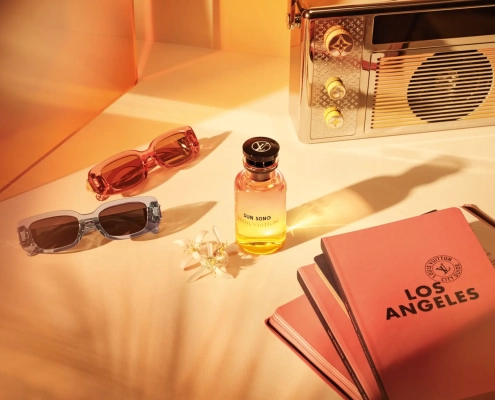 Parfumska voda Louis Vuitton Sun Song s sončno rumeno stekleničko, sončnimi očali in vodičem Los Angeles ob zlatem soncu. (David Magazine for Men with Style) / Louis Vuitton Sun Song perfume in a sunny yellow bottle, styled with sunglasses and a Los Angeles city guide under golden light. (David Magazine for Men with Style)