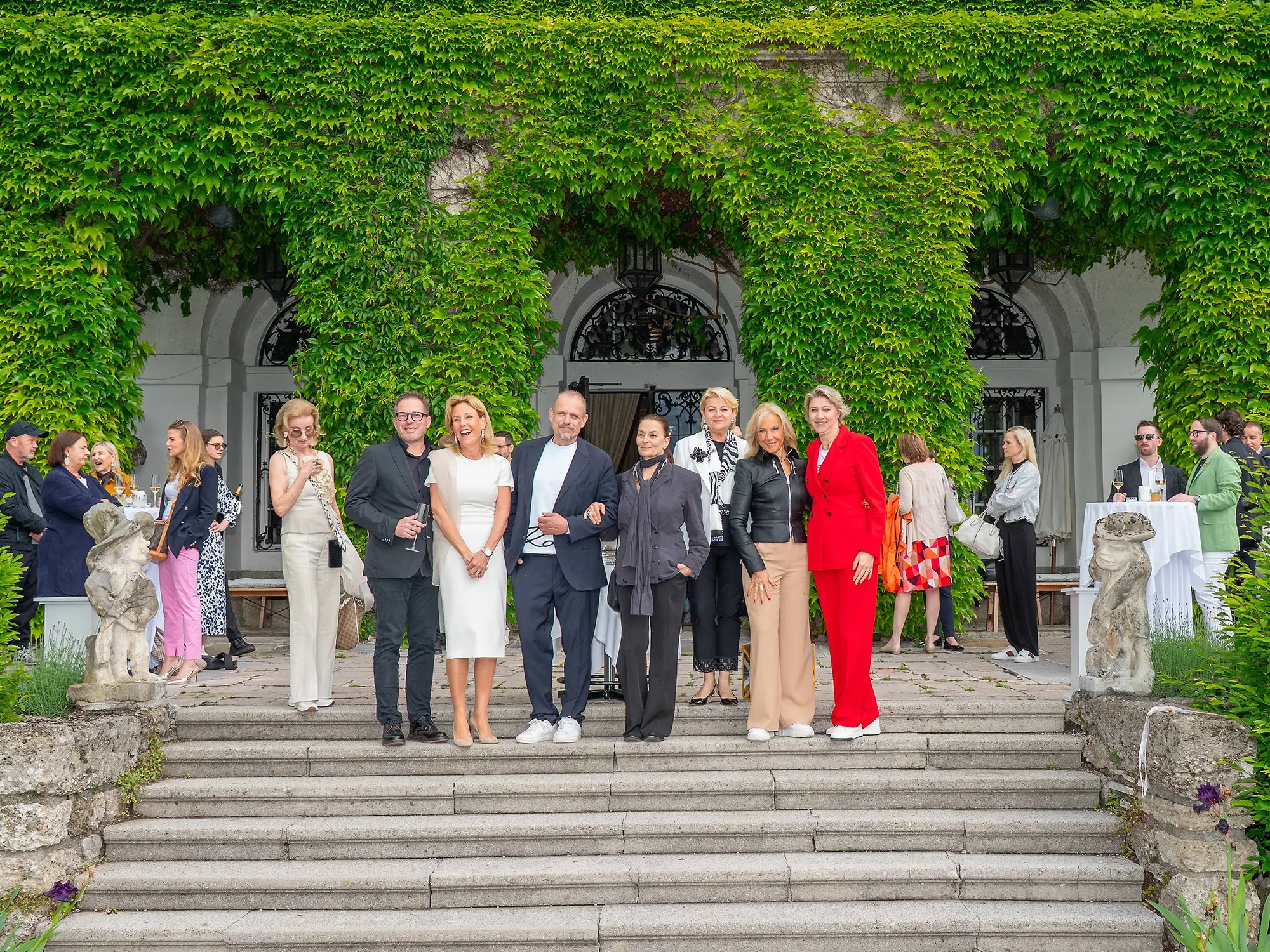 Skupina gostov na stopnišču gradu Leopoldskron na tiskovni konferenci pred prvim amfAR Gala Salzburg 2025; med njimi Gery Keszler, Arabel von Karajan, Elisabeth Gürtler, Marlies Muhr, Marion Pelzl, Elisabeth Friesacher in Mucky Degn. Prispevek revije David – revija za moške s stilom. / Guests gathered on the steps of Schloss Leopoldskron during the press event ahead of the inaugural amfAR Gala Salzburg 2025, including Gery Keszler and other supporters. Featured in David – men's magazine with style.