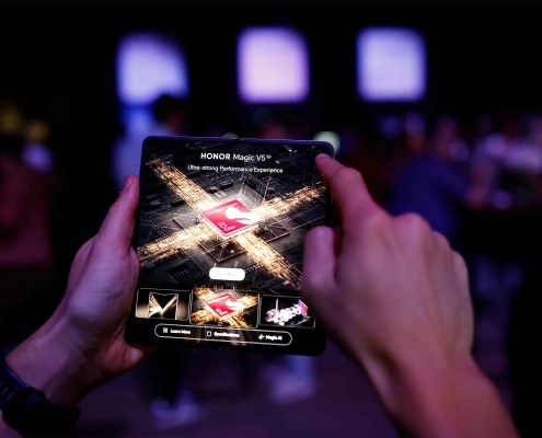 Obiskovalec uporablja zložljivi pametni telefon HONOR Magic V5 med premierno predstavitvijo v Ljubljani – tehnološka eleganca v rokah moškega s stilom. A visitor using the foldable smartphone HONOR Magic V5 during its premiere event in Ljubljana – technological elegance in the hands of a man with style.