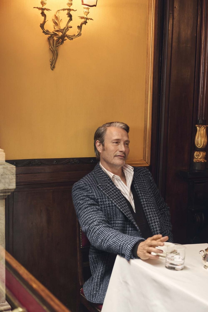 Igralec Mads Mikkelsen oblečen v elegantno pepita vzorčasto ZEGNA obleko, sedi v klasični italijanski kavarni in pije kavo – sofisticirana interpretacija torinskega stila za jesen/zimo 2025.
Actor Mads Mikkelsen wearing an elegant houndstooth ZEGNA suit, seated in a classic Italian café sipping coffee – a sophisticated take on the Turin style for Fall/Winter 2025.