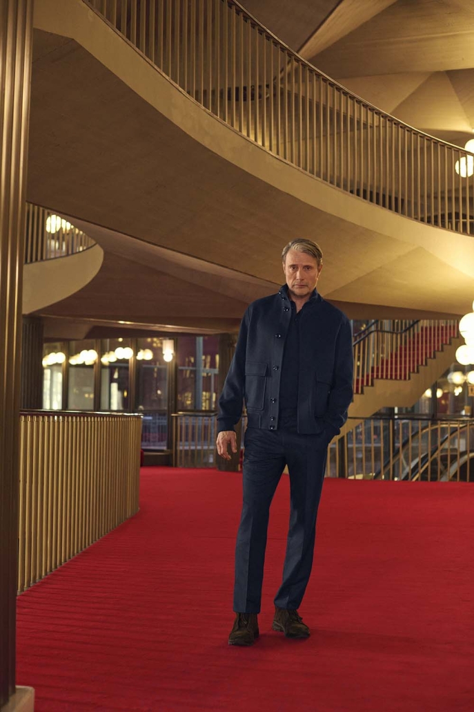 Igralec Mads Mikkelsen oblečen v elegantno pepita vzorčasto ZEGNA obleko, sedi v klasični italijanski kavarni in pije kavo – sofisticirana interpretacija torinskega stila za jesen/zimo 2025.
Actor Mads Mikkelsen wearing an elegant houndstooth ZEGNA suit, seated in a classic Italian café sipping coffee – a sophisticated take on the Turin style for Fall/Winter 2025.