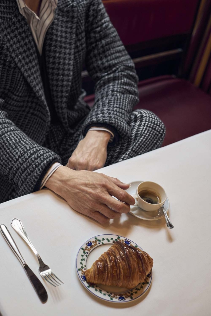 Igralec Mads Mikkelsen oblečen v elegantno pepita vzorčasto ZEGNA obleko, sedi v klasični italijanski kavarni in pije kavo – sofisticirana interpretacija torinskega stila za jesen/zimo 2025.
Actor Mads Mikkelsen wearing an elegant houndstooth ZEGNA suit, seated in a classic Italian café sipping coffee – a sophisticated take on the Turin style for Fall/Winter 2025.