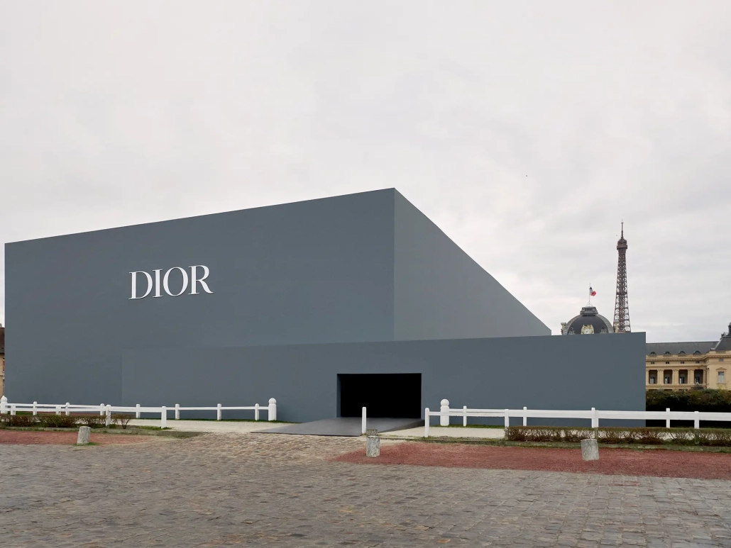 Zunanjost prizorišča modne revije Christian Dior jesen/zima 2025–2026 v Parizu, z moderno geometrično stavbo in razgledom na Eifflov stolp. Exterior of the Christian Dior Fall/Winter 2025–2026 fashion show venue in Paris, featuring a modern geometric structure and view of the Eiffel Tower.