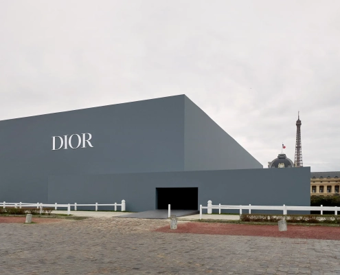 Zunanjost prizorišča modne revije Christian Dior jesen/zima 2025–2026 v Parizu, z moderno geometrično stavbo in razgledom na Eifflov stolp. Exterior of the Christian Dior Fall/Winter 2025–2026 fashion show venue in Paris, featuring a modern geometric structure and view of the Eiffel Tower.