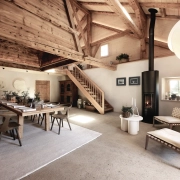Notranjost tradicionalne švicarske alpske koče Le Chalet z lesenim stropom, velikim jedilnim prostorom in sodobnim kaminom – prostor miru in prestiža, ki ga je obnovila urarska hiša Jaeger-LeCoultre. Interior of the traditional Swiss alpine chalet Le Chalet featuring wooden beams, a grand dining area and modern fireplace – a serene and refined retreat restored by the watchmaking house Jaeger-LeCoultre.