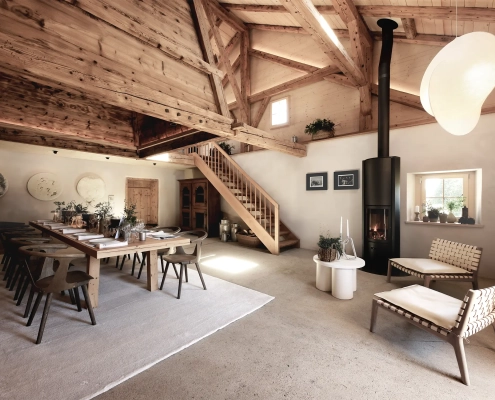 Notranjost tradicionalne švicarske alpske koče Le Chalet z lesenim stropom, velikim jedilnim prostorom in sodobnim kaminom – prostor miru in prestiža, ki ga je obnovila urarska hiša Jaeger-LeCoultre. Interior of the traditional Swiss alpine chalet Le Chalet featuring wooden beams, a grand dining area and modern fireplace – a serene and refined retreat restored by the watchmaking house Jaeger-LeCoultre.