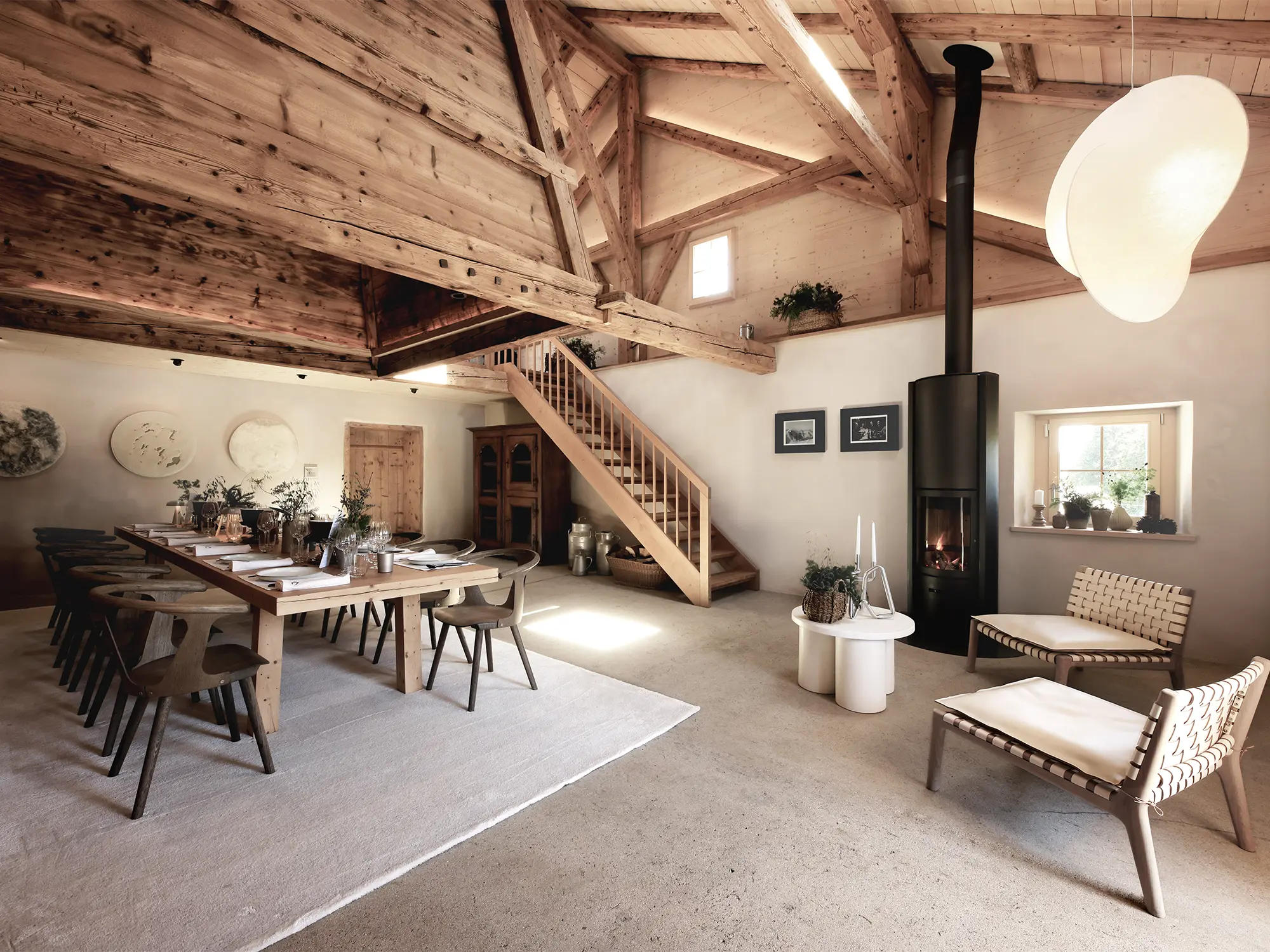 Notranjost tradicionalne švicarske alpske koče Le Chalet z lesenim stropom, velikim jedilnim prostorom in sodobnim kaminom – prostor miru in prestiža, ki ga je obnovila urarska hiša Jaeger-LeCoultre. Interior of the traditional Swiss alpine chalet Le Chalet featuring wooden beams, a grand dining area and modern fireplace – a serene and refined retreat restored by the watchmaking house Jaeger-LeCoultre.