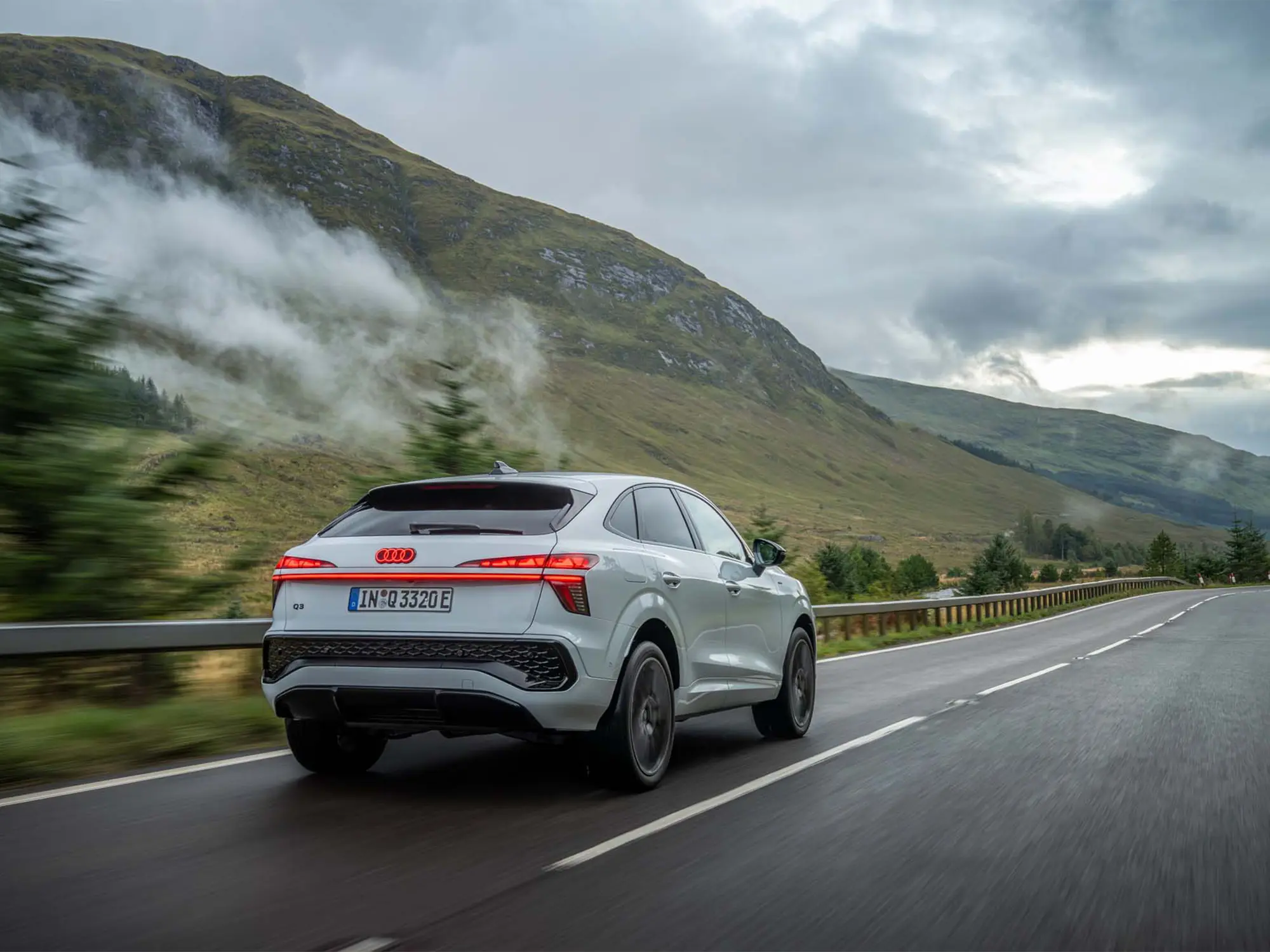 Novi Audi Q3 2025 vozi po mokri gorski cesti, obdani z meglo in zelenjem.