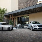 Audi Concept C med klasičnim dirkalnikom Silver Arrow in prvim Audijem TT pred sodobno arhitekturo – predstavitev električnega športnega koncepta.