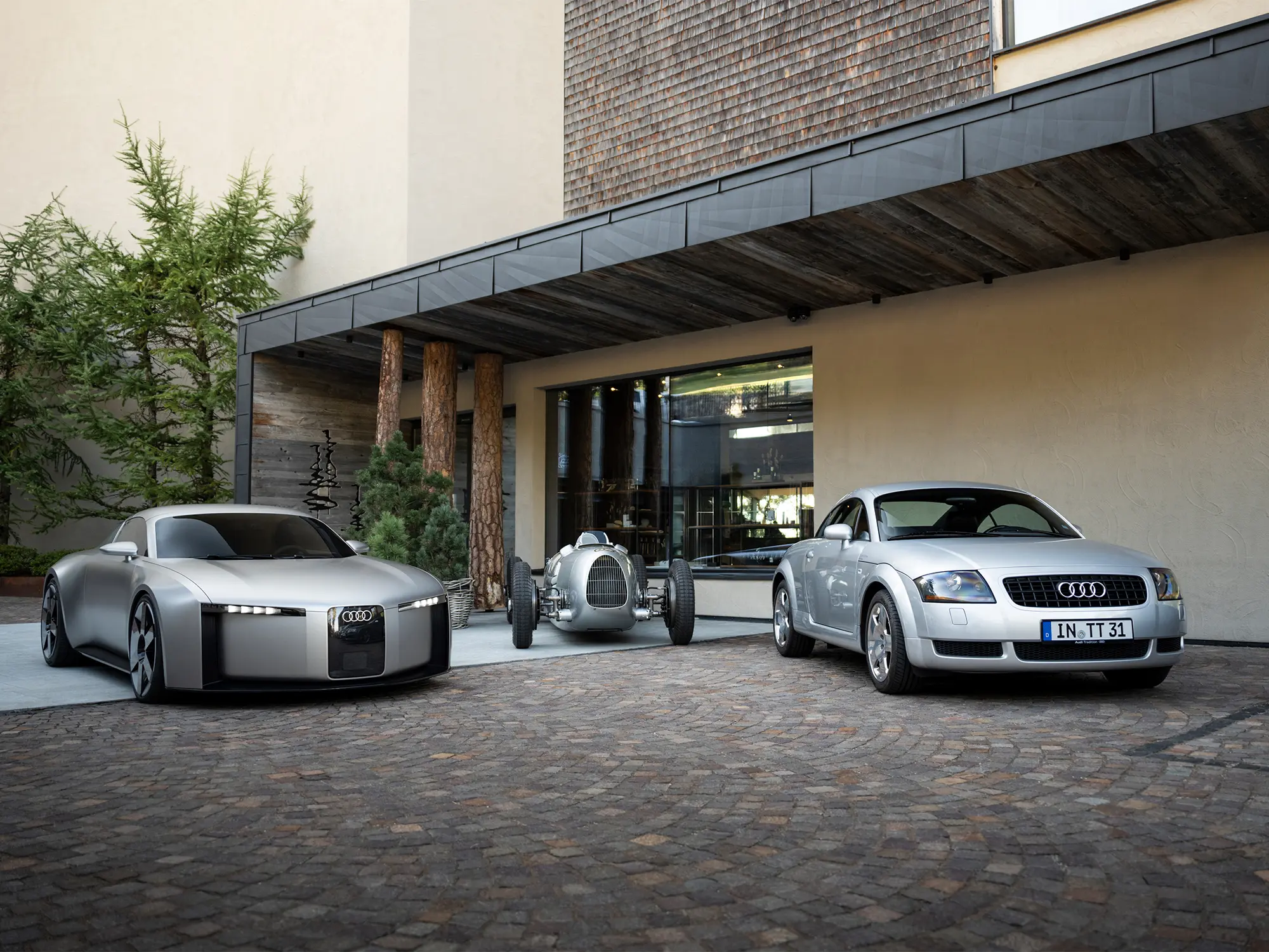 Audi Concept C med klasičnim dirkalnikom Silver Arrow in prvim Audijem TT pred sodobno arhitekturo – predstavitev električnega športnega koncepta.