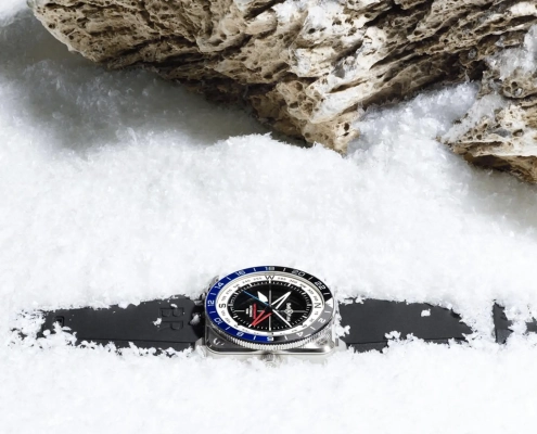 Instrumentna ura Bell & Ross BR-03 GMT z dvobarvno luneto in številčnico v obliki kompasa, položena v sneg.