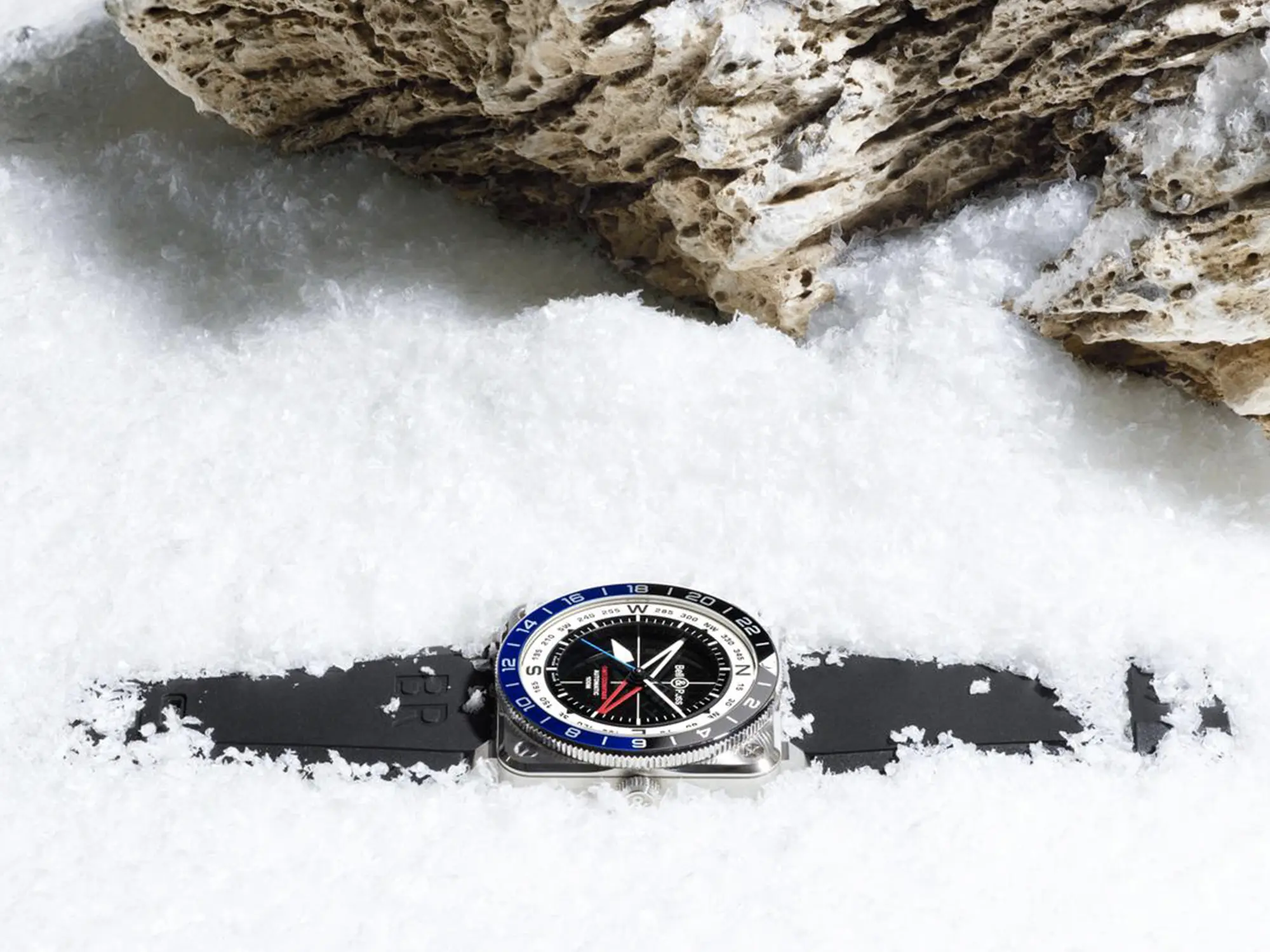 Instrumentna ura Bell & Ross BR-03 GMT z dvobarvno luneto in številčnico v obliki kompasa, položena v sneg.