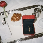 Eleganten zajtrk na srebrnem pladnju z rdečo Cartier škatlico, v kateri je zapestnica Cartier Love, ob kroasanu, skodelici in kovinski posodici za kavo.