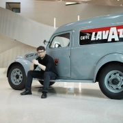 Industrijski oblikovalec Florian Seidl sedi ob klasičnem dostavnem vozilu Lavazza v sodobnem interierju.