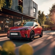 Rdeči Lexus LBX Vibrant Edition je parkiran pred sodobnim lokalom ob sončnem zahodu, ki poudari njegove športne linije in drzen videz.