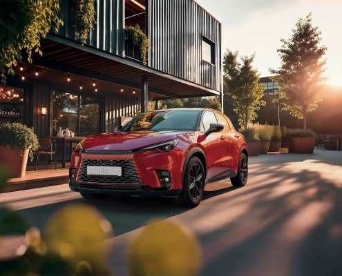 Rdeči Lexus LBX Vibrant Edition je parkiran pred sodobnim lokalom ob sončnem zahodu, ki poudari njegove športne linije in drzen videz.