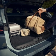 Oseba nalaga potovalno torbo v prostoren prtljažnik novega Peugeota 308 SW, v katerem sta tudi kovček in odeja.