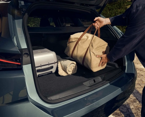 Oseba nalaga potovalno torbo v prostoren prtljažnik novega Peugeota 308 SW, v katerem sta tudi kovček in odeja.