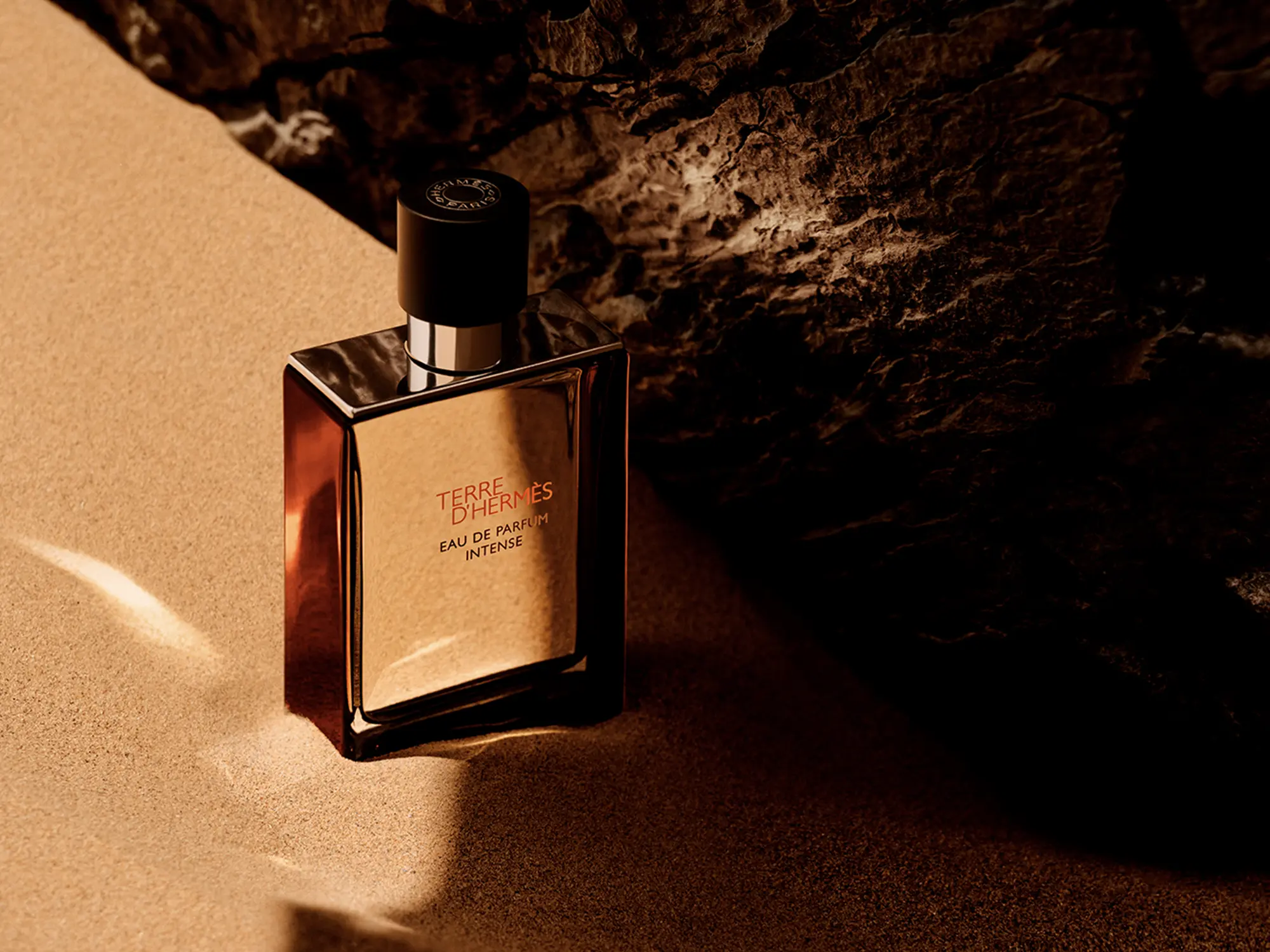 Terre d’Hermès Eau de Parfum Intense steklenička na pesku ob kamnu.