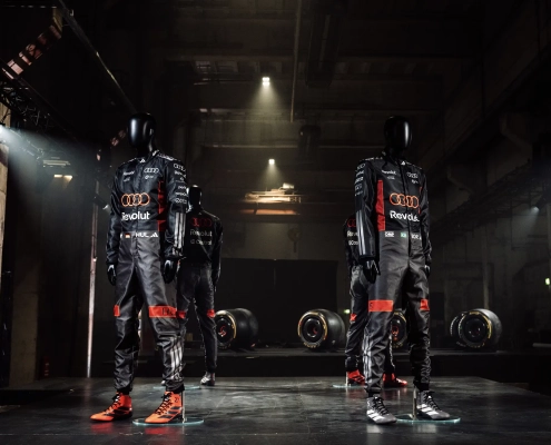 KO DIRKANJE NAVDIHNE MODO: GLOBALNA KOLEKCIJA ADIDAS X AUDI Ko se svet Formule 1 sreča z uličnim stilom, rezultat ni zgolj navijaška kolekcija, temveč modna izjava. Nova kolekcija adidas x Audi Revolut F1 Team je prav to – premišljeno oblikovan spoj vrhunskega motošporta, sodobne estetike in funkcionalne mode, ki briše meje med dirkališčem in mestnim asfaltom. To ni le oblačilo za navijače, temveč garderoba za tiste, ki Formulo 1 ne spremljajo samo ob nedeljah, ampak jo živijo kot del identitete. Sodelovanje med znamkama adidas in Audi v okviru projekta Audi Revolut F1 Team prinaša kolekcijo, ki deluje samozavestno, tehnično in presenetljivo elegantno. Že na prvi pogled je jasno, da ne gre za klasično »merch« linijo s kričečimi logotipi, temveč za sodobno športno modo, ki se brez težav znajde tako v paddocku kot na mestnih ulicah Milana, Berlina ali Ljubljane. Barvna paleta kolekcije je umirjena, a izrazito prepoznavna. V ospredju so sofisticirani sivo-krem odtenki, ki črpajo navdih iz titanium barve Audijevega dirkalnika, dopolnjujejo pa jih natančno odmerjeni rdeči poudarki. Ta kontrast ustvarja vizualno napetost – dovolj subtilno za vsakodnevno nošenje, a dovolj drzno, da jasno sporoča pripadnost svetu najvišjega razreda motošporta. Kolekcija ne kriči po pozornosti, temveč jo pridobi z detajli.
