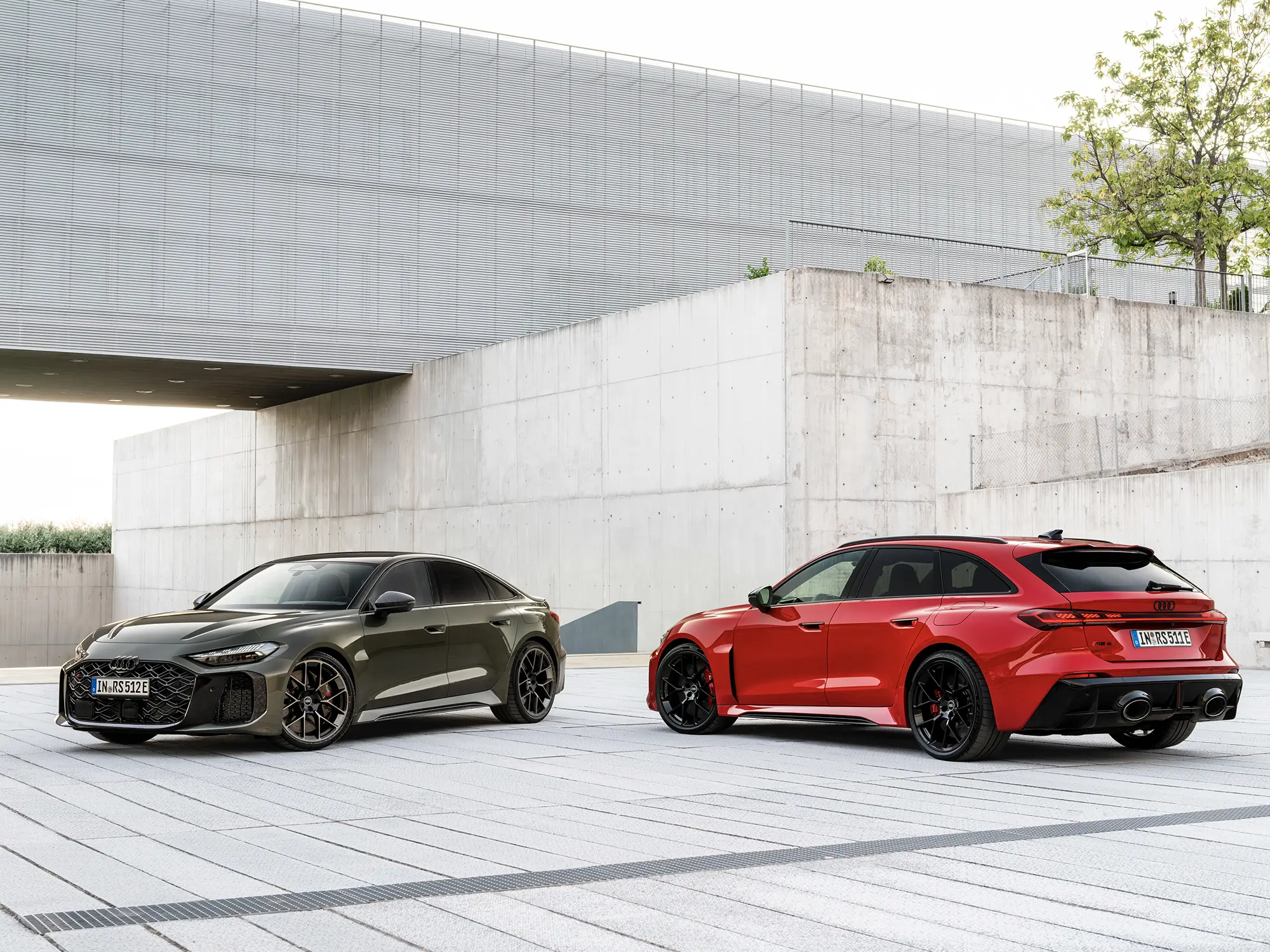 Audi RS 5 v sivi in rdeči barvi, parkiran pred moderno arhitekturo.