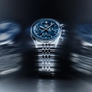 TAG Heuer Carrera kronograf z modro številčnico in jekleno zapestnico v dinamični svetlobni kompoziciji.